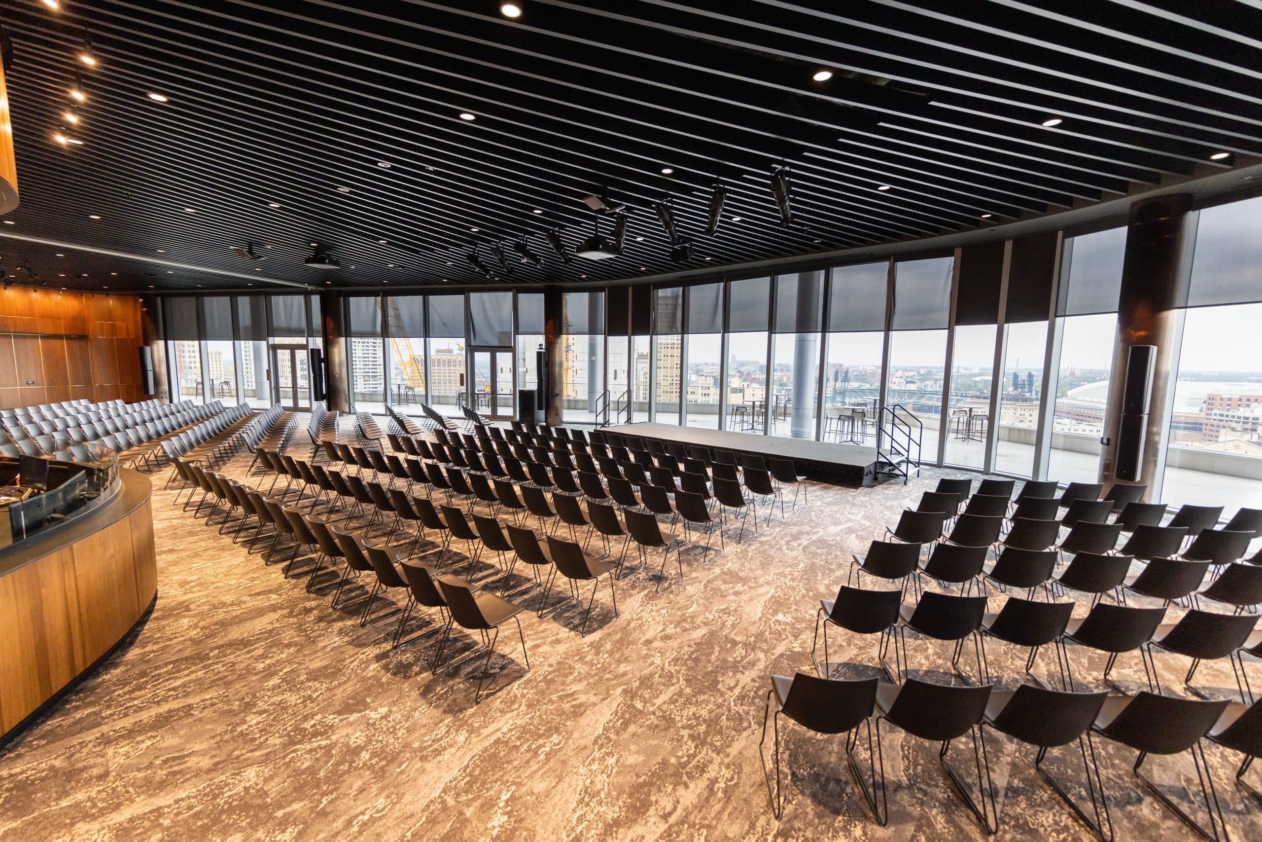 Theatre style seating facing portable stage and floor to ceiling windows with view of terrace of Elevate at One Campus Martius overlooking the city of Detroit.